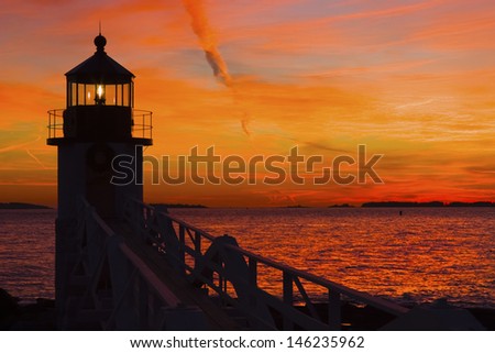 Marshall Point Lighthouse with orange sky at sunset on the coast of Maine.