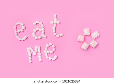 Marshmallows on pink background with sign in English Eat me. Flat lay or top view. Background or texture of colorful mini marshmallows. Winter food background concept