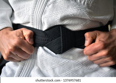 Martial artist is tying black belt, clenched fists are making flat knot