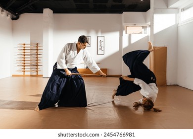 A martial artist in a white gi executes an aikido technique with a jo staff, causing their partner in a black hakama to perform a controlled flip. Text: "Aikido" - Powered by Shutterstock