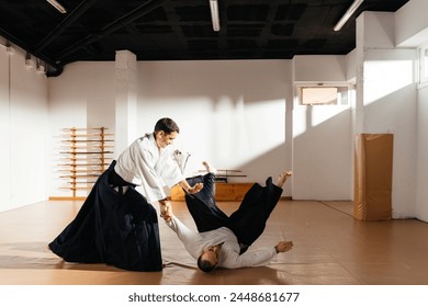 A martial artist in a white gi performs a precise throw on an opponent, who falls onto a well-lit dojo mat. - Powered by Shutterstock