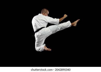 Martial arts aesthetic. In a jump. Young karate sportsman training isolated over black background. Man standing in karate side kick. Concept of martial art, combat sport, energy, fit, ad