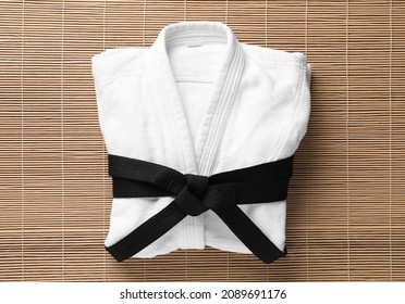 Martial arts uniform with black belt on bamboo mat, top view