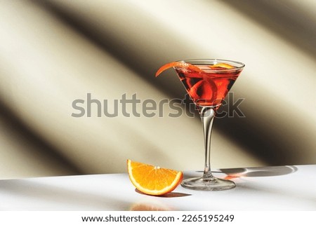 Martinez alcoholic cocktail drink with red vermouth, liqueur, orange bitter, zest and ice. Light beige background, hard light, shadow pattern, copy space
