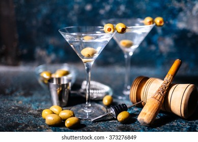 Martini cocktail drink with olives garnish and tools on rusty background