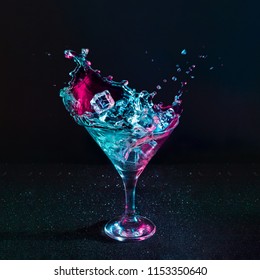 Martini Cocktail Drink Splash With Ice Cubes In Neon Iridescent Pink And Blue Colors. Minimal Night Party Life Concept.