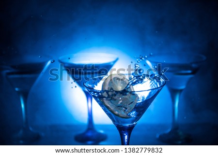 Martini cocktail glass splashing on dark toned smoky background or colorful cocktail in glass with splashes and lemon. Party club entertainment. Mixed light. Selective focus