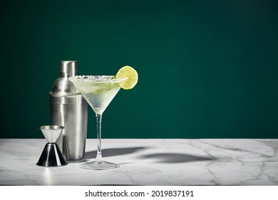 Martini cocktail with ice and slice of lime, and shaker on a marble table. An alcoholic cocktail or non-alcoholic mocktail