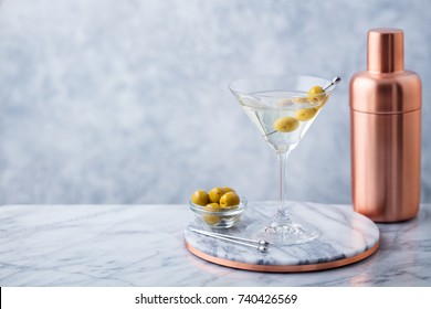 Martini cocktail with olives and bar shaker on marble table background. Copy space.