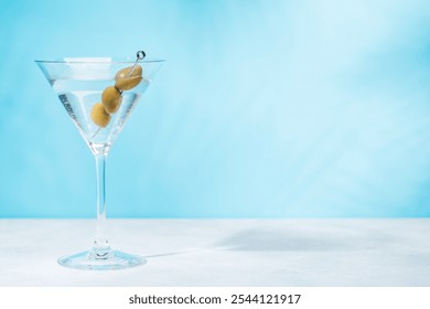 A martini cocktail on a table against a light blue background, enhanced by sunny glares and playful shadows - Powered by Shutterstock