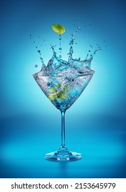 Martini Glass With Amazing Splash As The Result Of Olive Berries Falling Down In It. Blue Background.