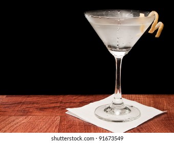 Martini on a bar garnished with a lemon twist isolated on a black background