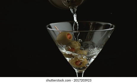 Martini is poured into a glass with olives
