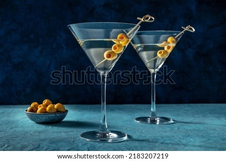 Martini, two glasses with spicy olives. Alcoholic cocktail on a blue background
