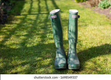Marylebone, London/UK - April 9 2020: Pair of green Hunter wellington boots on a green lawn in bright sunshine. The shadow of a fence is visible in the background. Lawn is neat. No people.