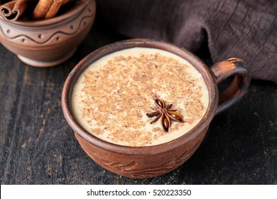 Masala tea chai latte traditional hot Indian sweet milk spiced drink, ginger, fresh spices blend organic infusion healthy wellness beverage in rustic clay cup on dark table background