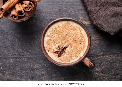 Masala tea chai latte traditional warm Indian sweet milk spiced drink, ginger, cinammon sticks, fresh spices blend organic infusion healthy wellness beverage in rustic clay cup on dark table
