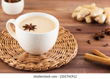 Masala tea with milk, anise, cinnamon, ginger, pepper in a cup on a wooden table. Selective focus.