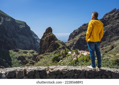 Masca Canyon in the mountain municipality in Tenerife, Canary Islands. Tourist man middle aged enjoys the view of village, rock gorge and peaks of the mountain ranges. Touristic destination. Travel. - Shutterstock ID 2228568891