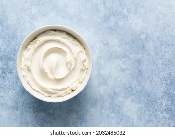 Mascarpone cheese (or cream cheese, ricotta) in white ceramic bowl top view. Ingredient for cooking italian dessert tiramisu. Creamy texture. Copy space. Blue concrete background. 