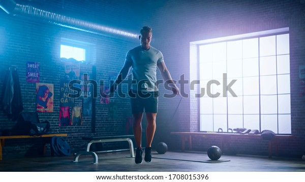 Masculine
Athletic Young Man Exercises with Jumping Rope in a Loft Style
Industrial Gym. He's Doing His Intense  Fitness Training Program.
Facility has Motivational Posters on the
Wall.