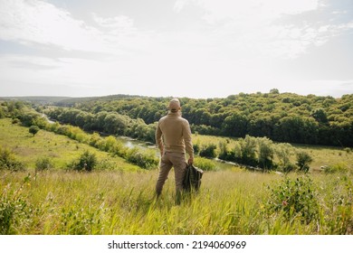 Masculine leisure concept: strong male figure back view with backpack stands on beautiful natural summer landscape outdoors - Shutterstock ID 2194060969
