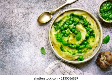 Mashed potato with pesto sauce and sweet pea in a bowl over light slate, stone or concrete background.Top view with copy space.