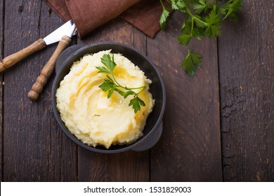 Mashed potatoes or boiled puree with parsley  in cast iron pot on dark wooden rustic background.  top view - Powered by Shutterstock