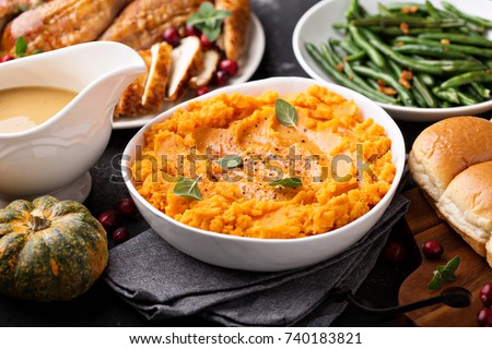 Mashed sweet potatoes with butter and cinnamon on Thanksgiving table with turkey and green beans