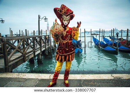 Mask and gondola. festive costume in red and yellow at the Venetian Carnival. In the background are gondolas on the water. mystical Venice. Venice without people. Venetian carnival without tourists