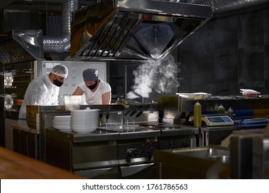 Mask On The Chef's Face In A Restaurant: Cooks In An Open Kitchen, A Client Sees Work During A Pandemic