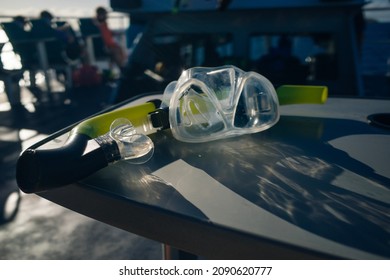 Mask And Scuba Diving Equipment On Wood Table In Caribbean Sea Wit Boat At Background