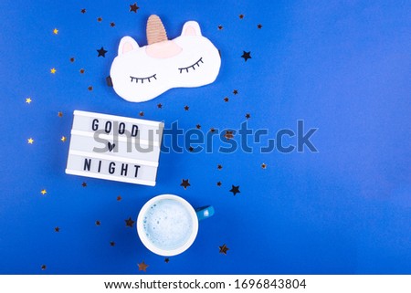 A mask for sleeping, a diary for notes and a cup of matches on a blue background. Evening routine before bedtime. Copy space.