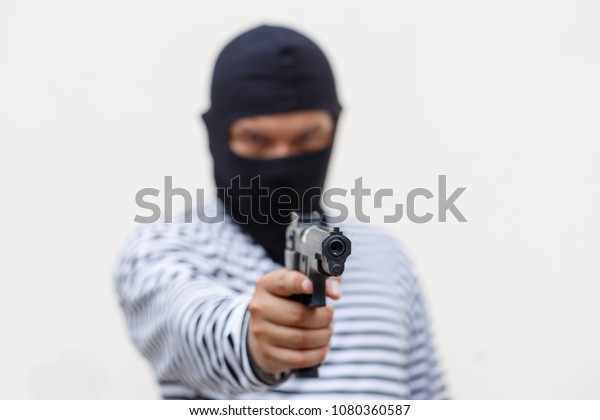 Mask thief in balaclava with\
holding gun. Outlaw bad man hold a gun pointing the target at\
restroom. robber in black hood holding gun and pointing to a\
person.