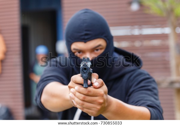 Mask thief in balaclava with holding gun.bad\
man hold a gun pointing the target at restroom. robber in black\
hood holding gun and pointing to a\
person.