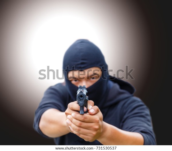 Mask thief in balaclava with holding gun.\
Outlaw bad man hold a gun pointing the target. robber in black hood\
holding gun and pointing to a\
person.