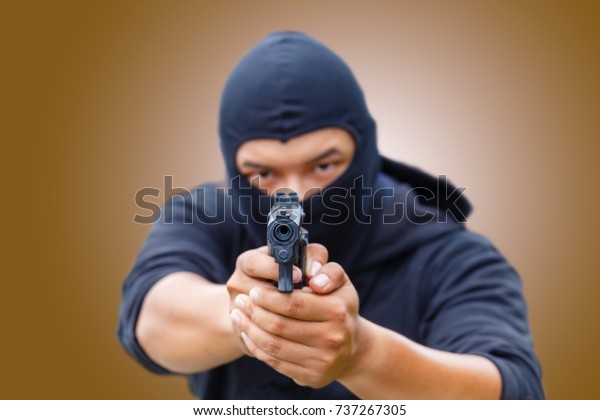 Mask thief in balaclava with\
holding gun. Outlaw bad man hold a gun pointing the target at\
restroom. robber in black hood holding gun and pointing to a\
person.