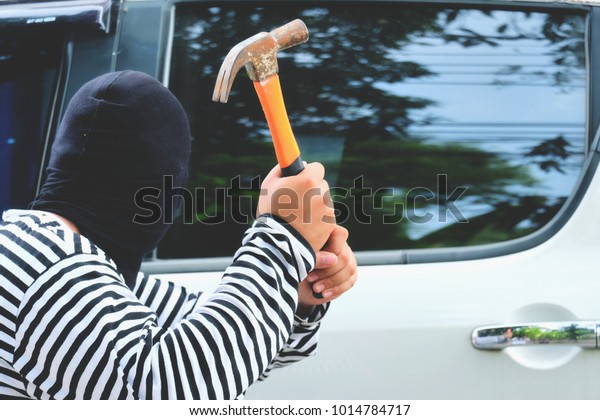 Mask\
thief in balaclava with holding hammer and trying  break into a\
car, Outlaw bad man hold  weapon and steal a\
car