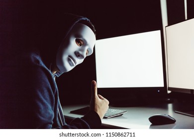 Masked And Anonymous Hacker Under Hood Giving Thumbs Up While Using A Computer With Empty Blank White Screen In The Dark Room - With Copy Space On Screen