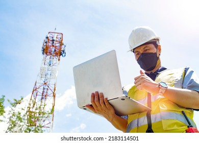 Masked asian male electrical engineer architect uses laptop to field work near telecommunication tower to inspect 5Gg telecommunication technology network tower network thumbs up confidently. - Shutterstock ID 2183114501