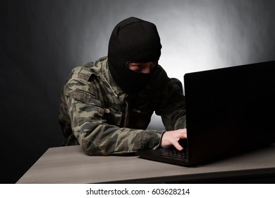 Masked Cyber Terrorist In Military Uniform Hacking On Dark Background.