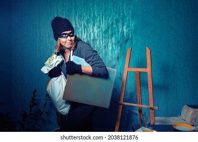 A Masked Female Robber Is Carrying A Stolen Bag Of Money And A Painting. The Background Is Dark Blue. The Concept Of Theft And Crime.