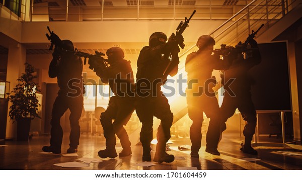Masked Fireteam of Armed SWAT Police Officers\
Storm a Sunny Seized Office Building with Desks and Computers.\
Soldiers with Rifles Move Forwards and Cover Surroundings. Shot\
with Yellow Warm Filter.