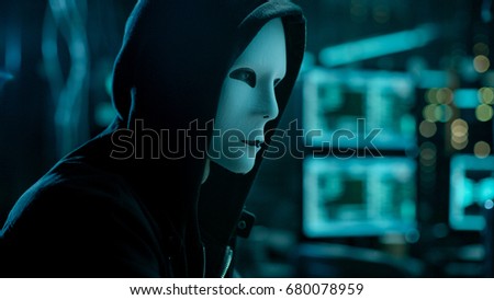 Masked Hacktivist Organizes malware Virus Attack on Global Scale. Hacker in Underground Secret Location Surrounded by Displays and Cables.