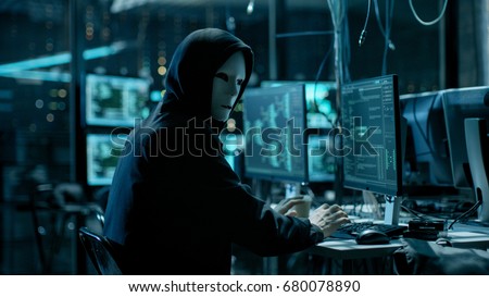 Masked Hacktivist Organizes Massive Data Breach Attack on Corporate Servers. He is in Underground Secret Location Surrounded by Displays and Cables.