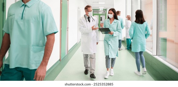 Masked healthcare professionals, including doctors and nurses, walk through a hospital hallway while discussing patient information on a tablet. Healthcare, teamwork, and medical technology themes. - Powered by Shutterstock