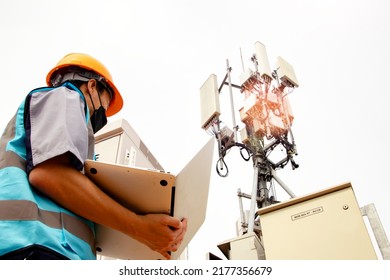 Masked Man Electronics Asian Worker  Skilled Control IT System, Control Cabinet, Station Telecommunication Tower Uses Laptop To Inspect 5G Network Technology Telecommunications Circuit Board System.
