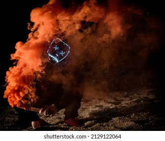 Masked Man Holding An Orange Smoke Bomb At Night.