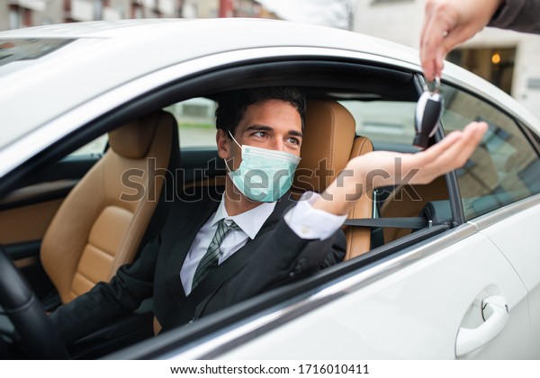 Masked man taking the car keys, automotive\
coronavirus concept