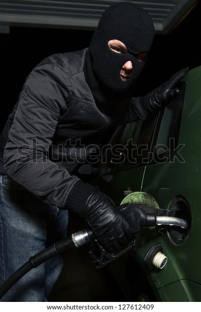 masked man using gas\
pump